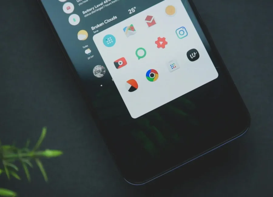 Close-up of a smart phone displaying various app icons on a dark background with greenery.